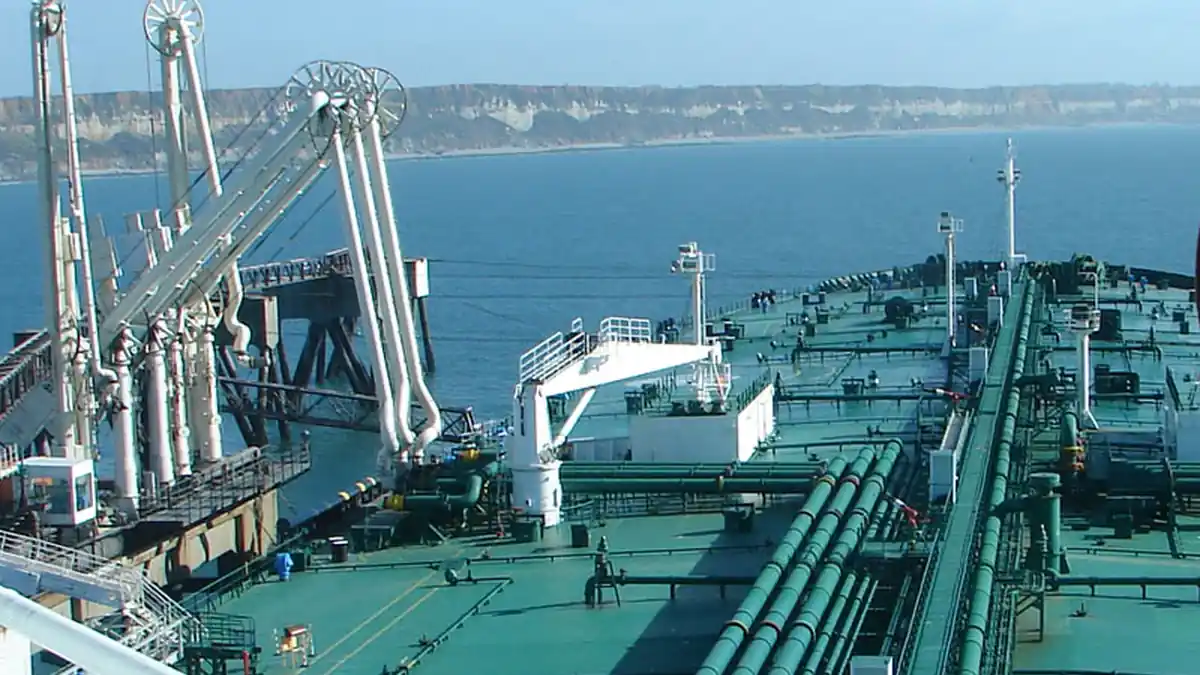 A large crude oil tanker unloading cargo at an industrial port, representing the class of vessel struck in the Strait of Hormuz