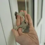 A hand holding a set of house keys beside a door lock, symbolizing a completed residential purchase.