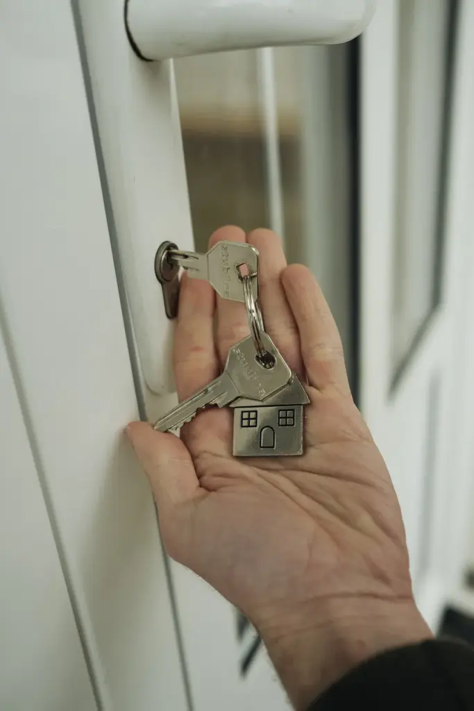 A hand holding a set of house keys beside a door lock, symbolizing a completed residential purchase.