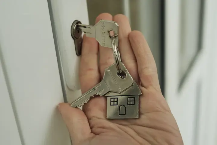 A hand holding a set of house keys beside a door lock, symbolizing a completed residential purchase.