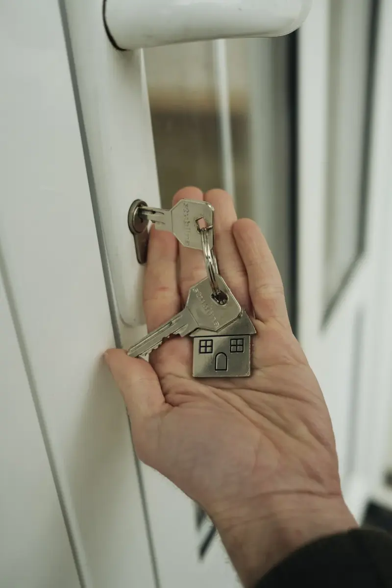 A hand holding a set of house keys beside a door lock, symbolizing a completed residential purchase.