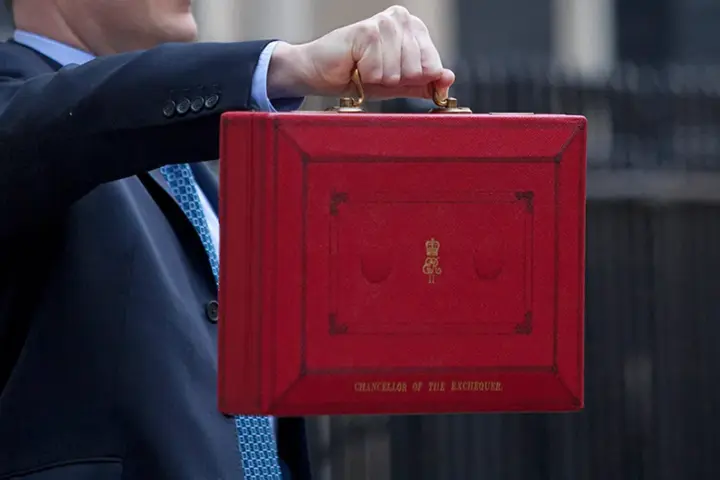 A government chancellor at a podium presenting the annual budget with fiscal documents visible