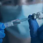 Medical practitioner preparing a measles vaccine dose using a sterile syringe and glass medication vial.