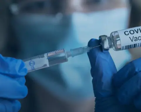 Medical practitioner preparing a measles vaccine dose using a sterile syringe and glass medication vial.