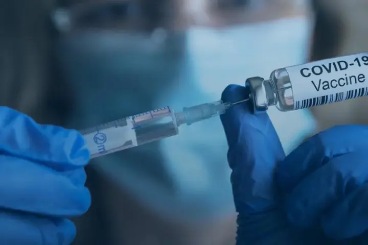 Medical practitioner preparing a measles vaccine dose using a sterile syringe and glass medication vial.