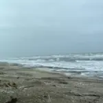 Storm waves crashing on a rocky Bering Sea coastline with driftwood and patches of snow on the beach