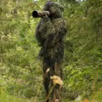 A wildlife photographer wearing a camouflage ghillie suit in a natural setting