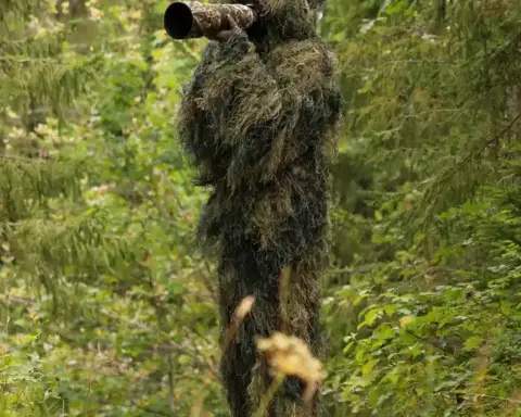A wildlife photographer wearing a camouflage ghillie suit in a natural setting