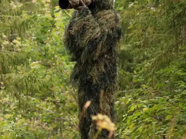 A wildlife photographer wearing a camouflage ghillie suit in a natural setting