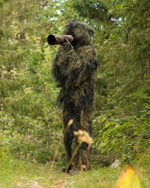A wildlife photographer wearing a camouflage ghillie suit in a natural setting