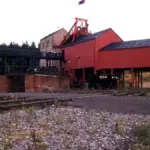 The red headframe and engine house of a former British coal mine, with railway sidings in the foreground.