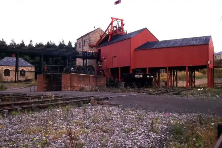The red headframe and engine house of a former British coal mine, with railway sidings in the foreground.